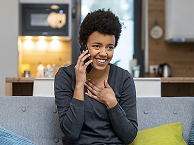 A woman smiles with her hand touching her chest as she talks on her cellphone in her home.