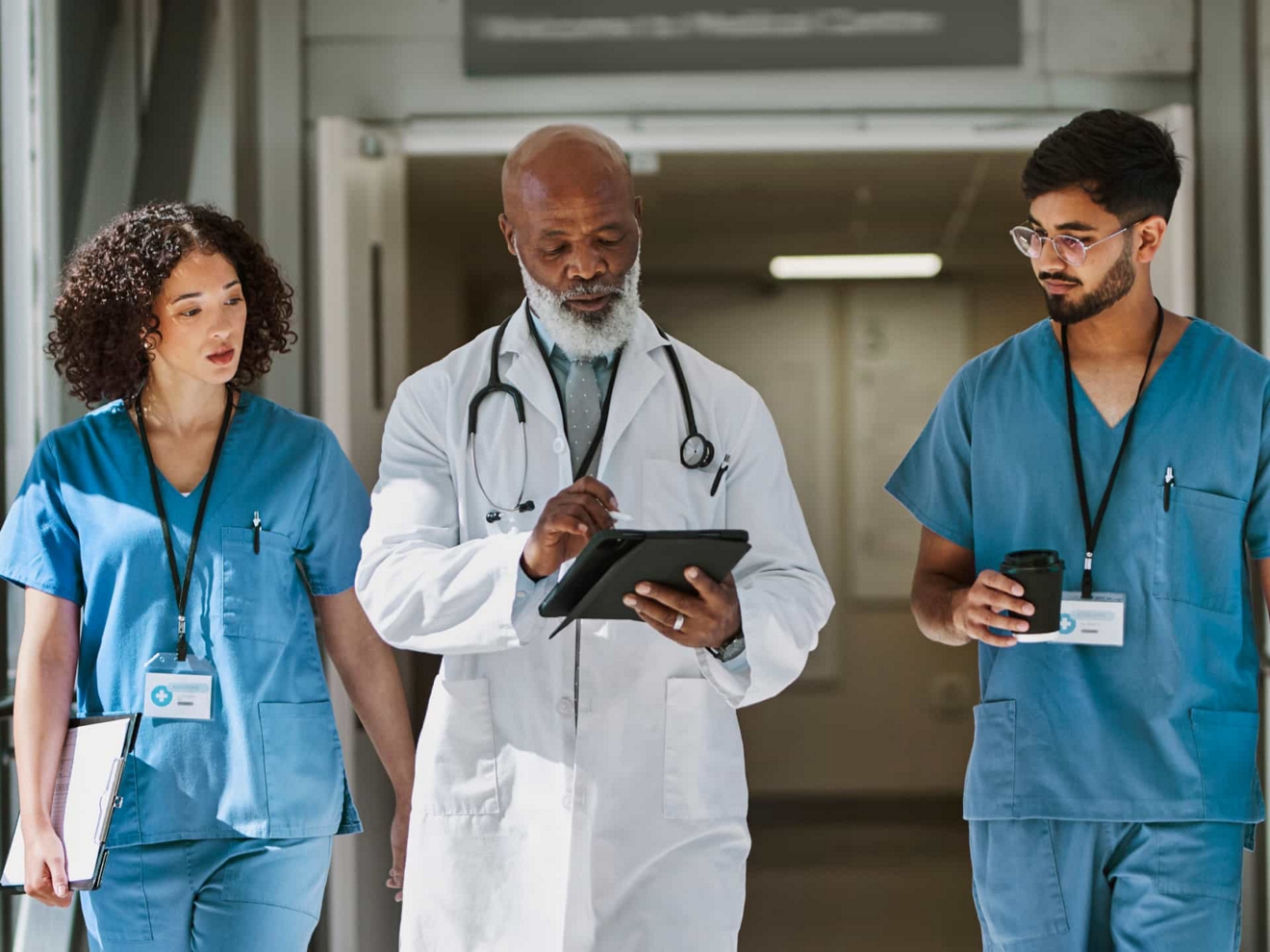 A doctor walks with colleagues down a hospital corridor and reviews information on a digital tablet.