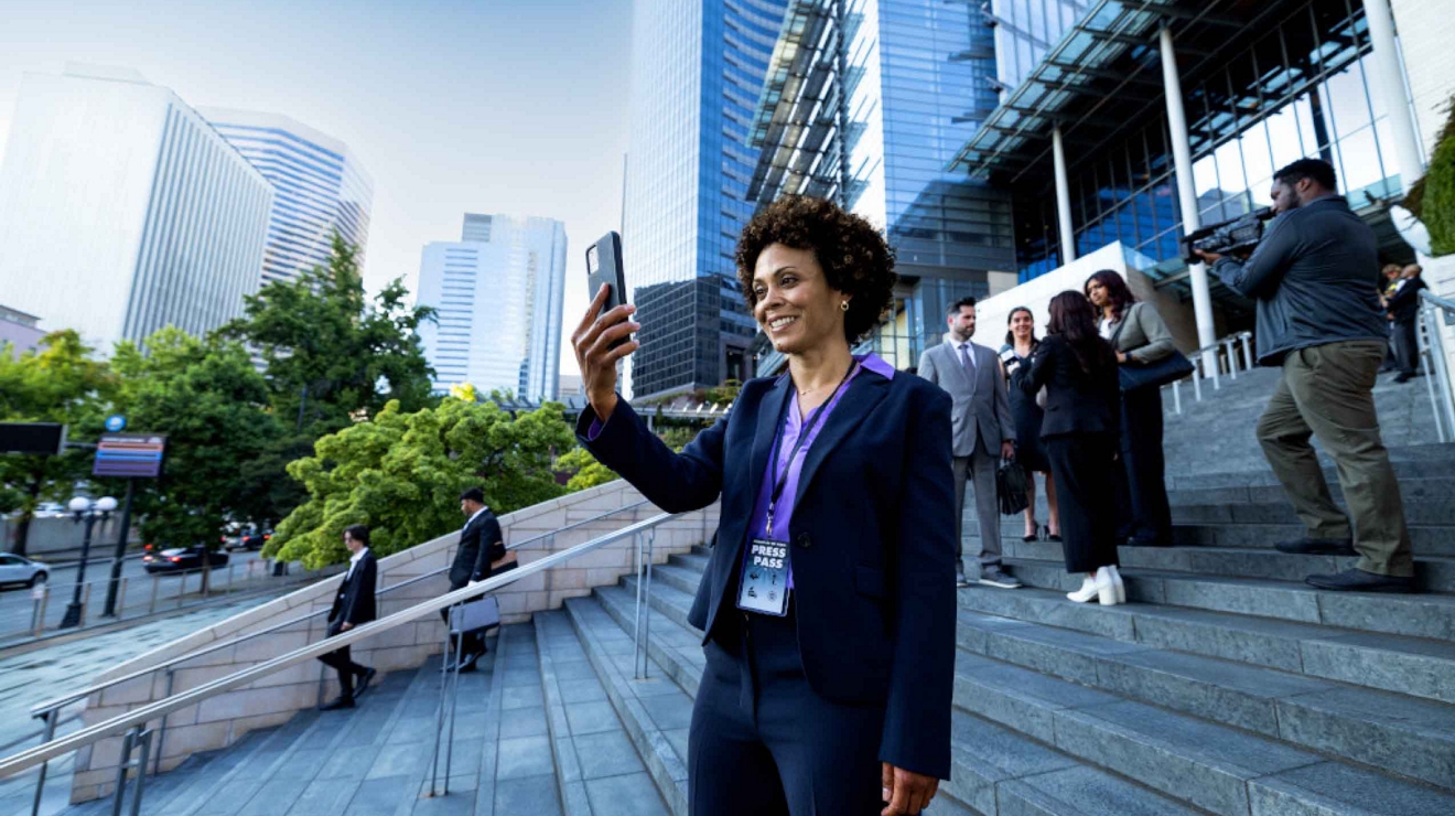 A journalist wearing a press pass outside a courthouse stays connected to colleagues on a mobile phone.