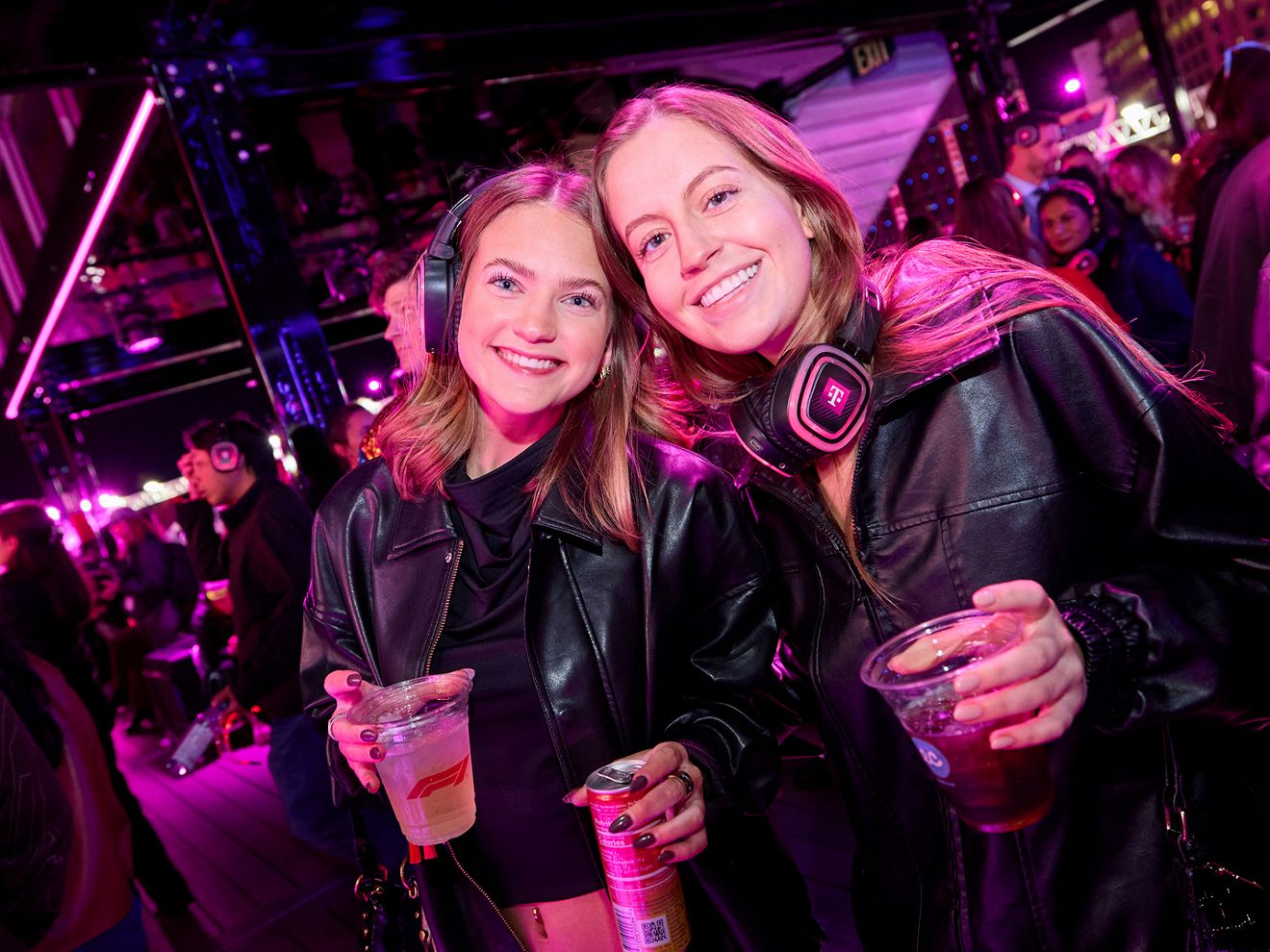 Two friends inside Club Magenta smiling at the camera with drinks in hand. 