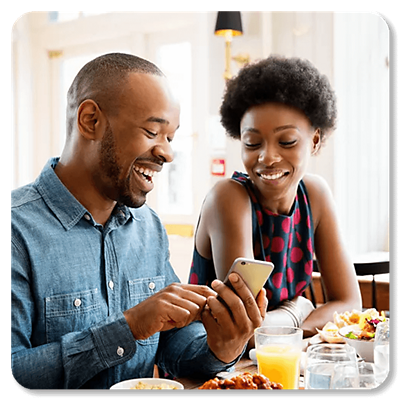 A couple laughing, looking at a phone while having a meal.