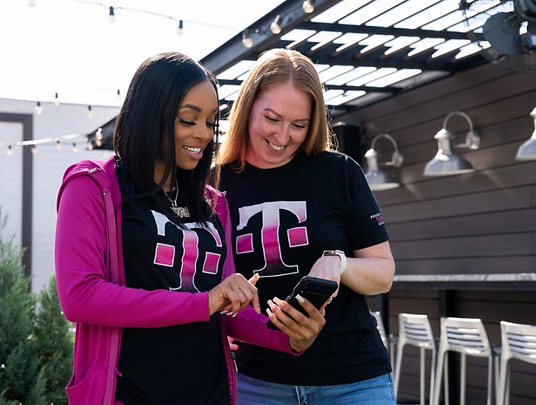 Two people outside in T-Mobile t-shirts looking at one person’s mobile phone