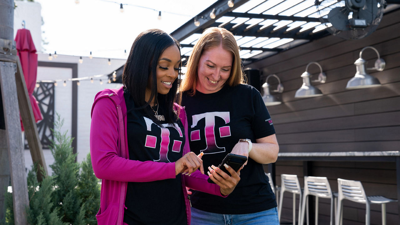Two smiling T-Mobile employees looking at a smart phone