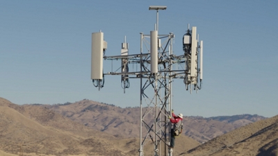 T-Mobile technician climbing a cell tower with mountains in the background