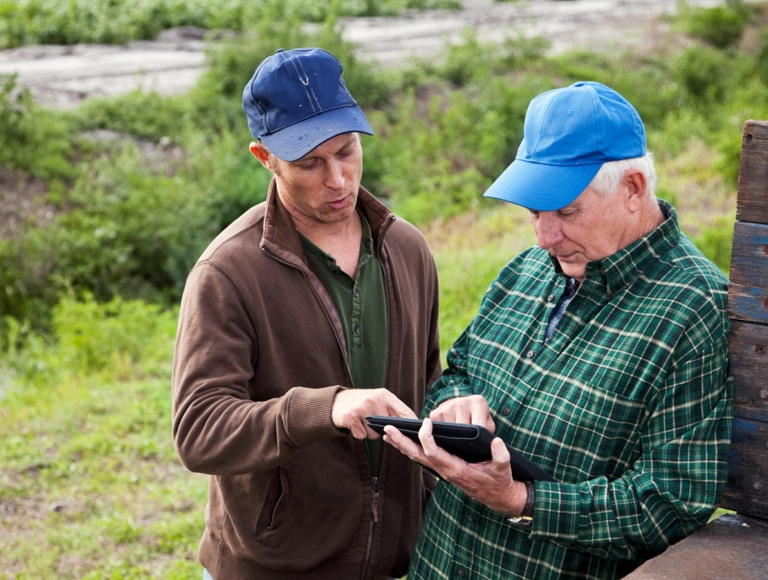 Two farmers working on a tablet near a truck bed