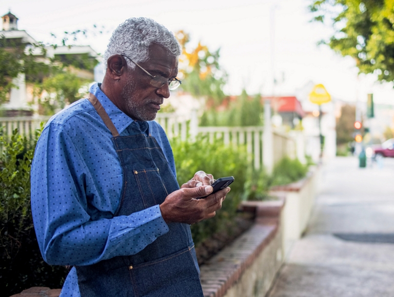 Shop worker using a smartphone on a city sidewalk