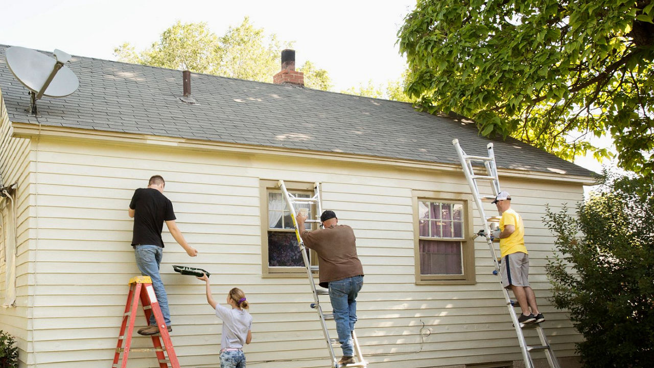 Group of people on ladders painting the exterior of a house