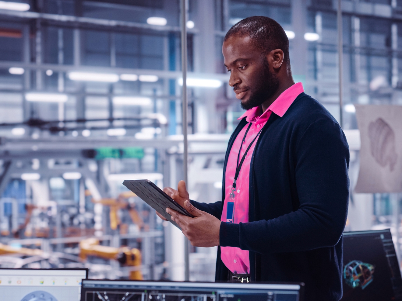 A man is wearing a magenta polo shirt in a lab. He smiles as he looks at his tablet. 