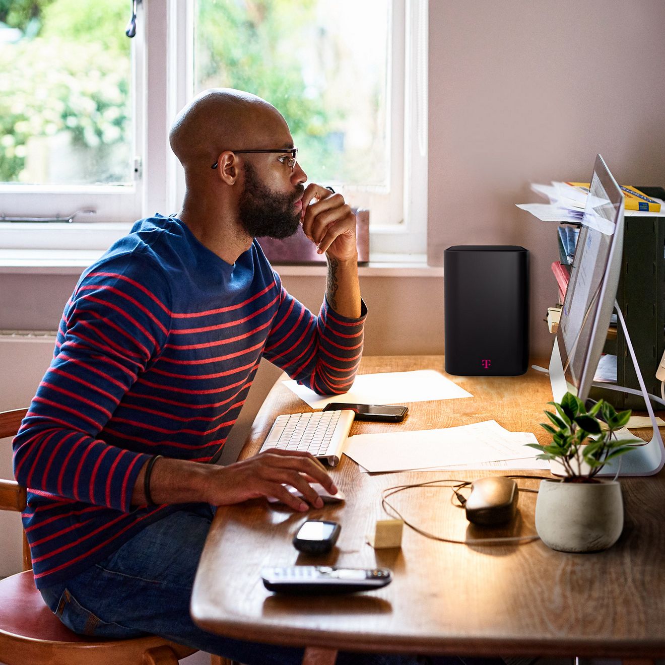 A man sits at a desk, working on a computer. A T-Mobile internet gateway sits nearby.