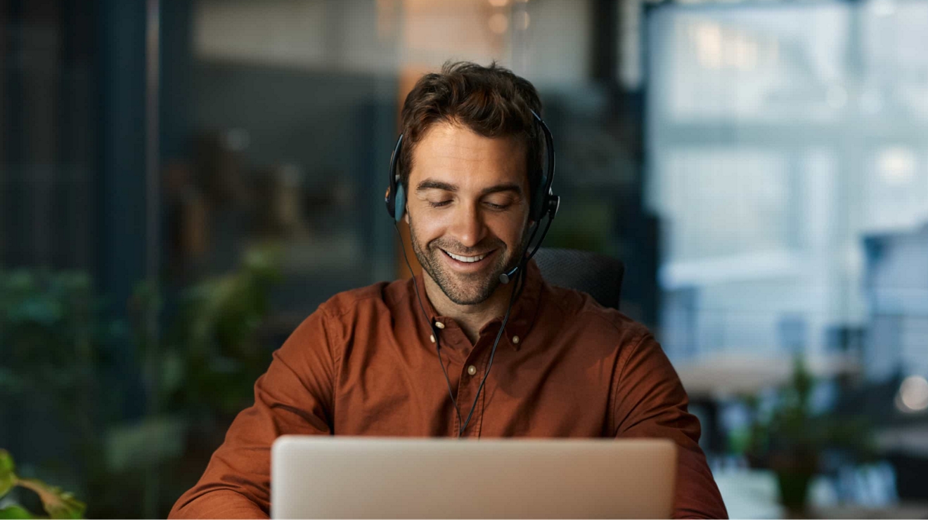 A government worker wears headphones while taking a conference call from a laptop.