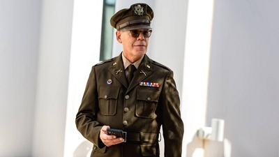 A uniformed officer walks with a mobile phone in their hands.