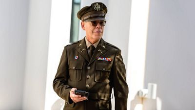 A uniformed officer walks with a mobile phone in their hands.