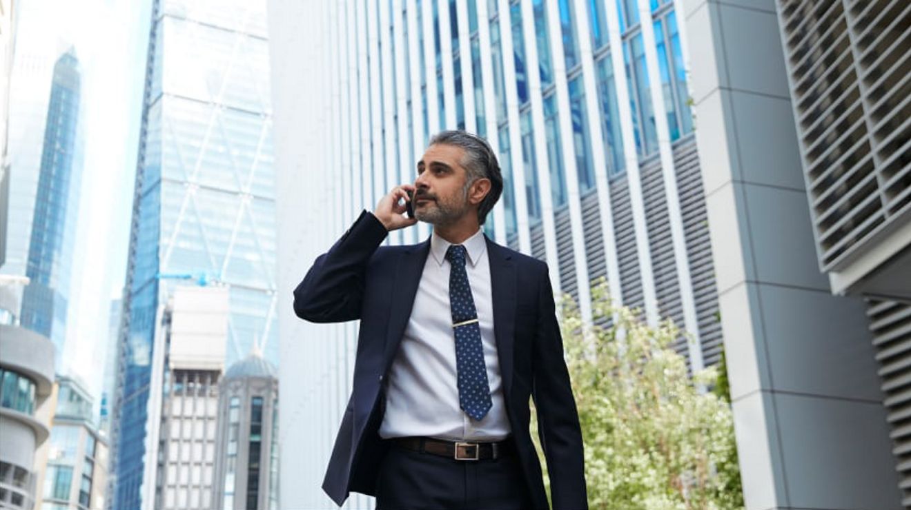 A business professional takes a phone call while walking through a corporate plaza.