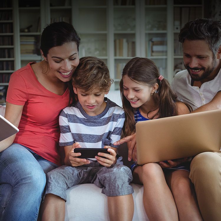 Una familia de cuatro sentada en un sofá mirando un smartphone.