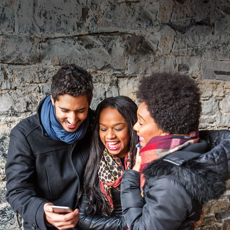 Un hombre y dos mujeres sonríen mirando un smartphone