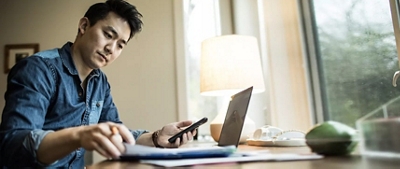 Un hombre usando su teléfono y laptop mientras trabaja.