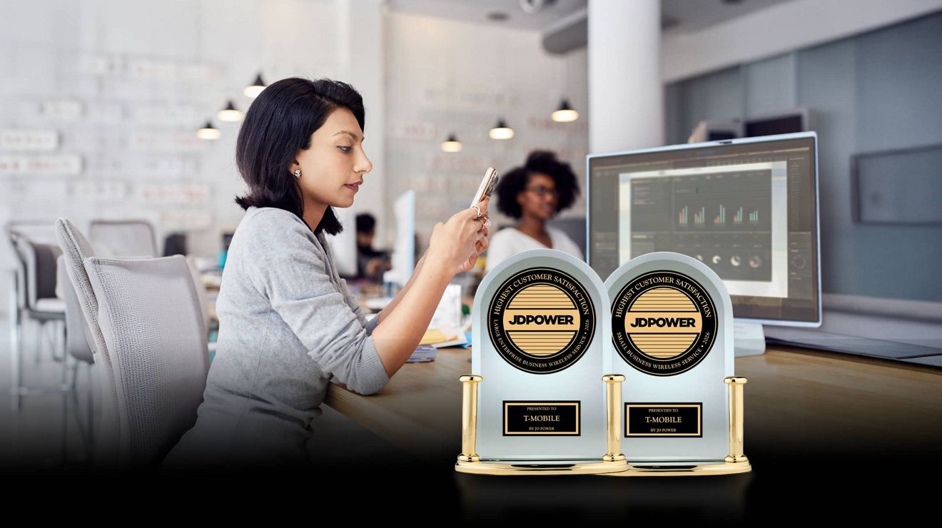 A business analyst uses a smartphone at their desk behind two JD Power Awards for business wireless customer satisfaction.