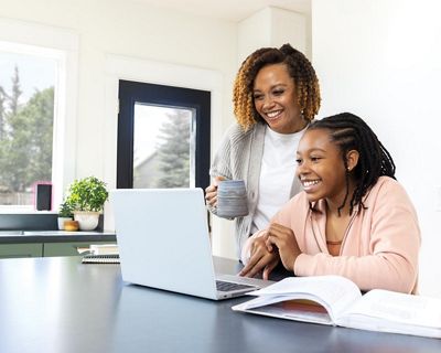 A woman and a young girl focused on a laptop screen, engaged in a shared digital experience.