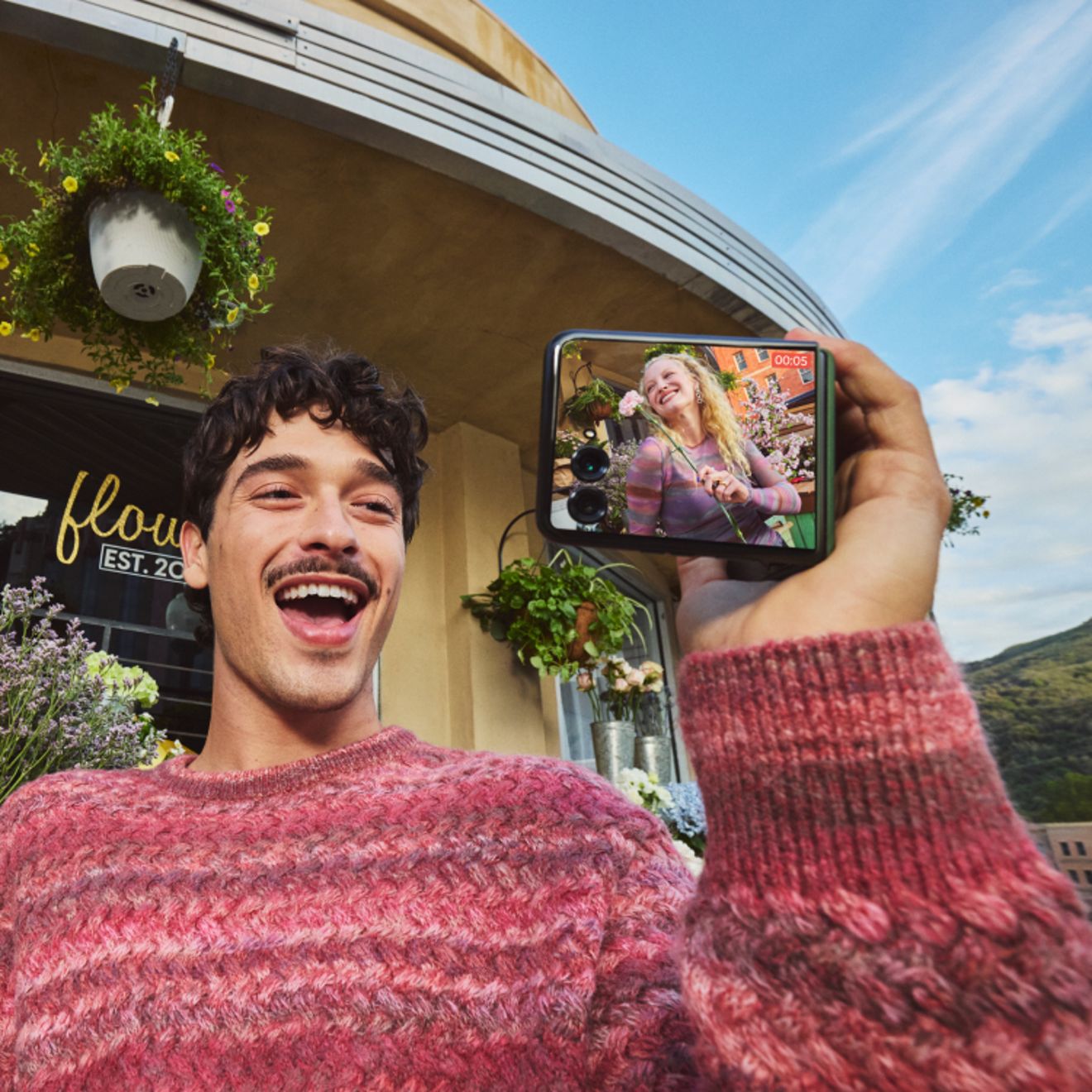 Person taking a selfie outdoors with a motorola razr, smiling while using the external display to preview the photo.