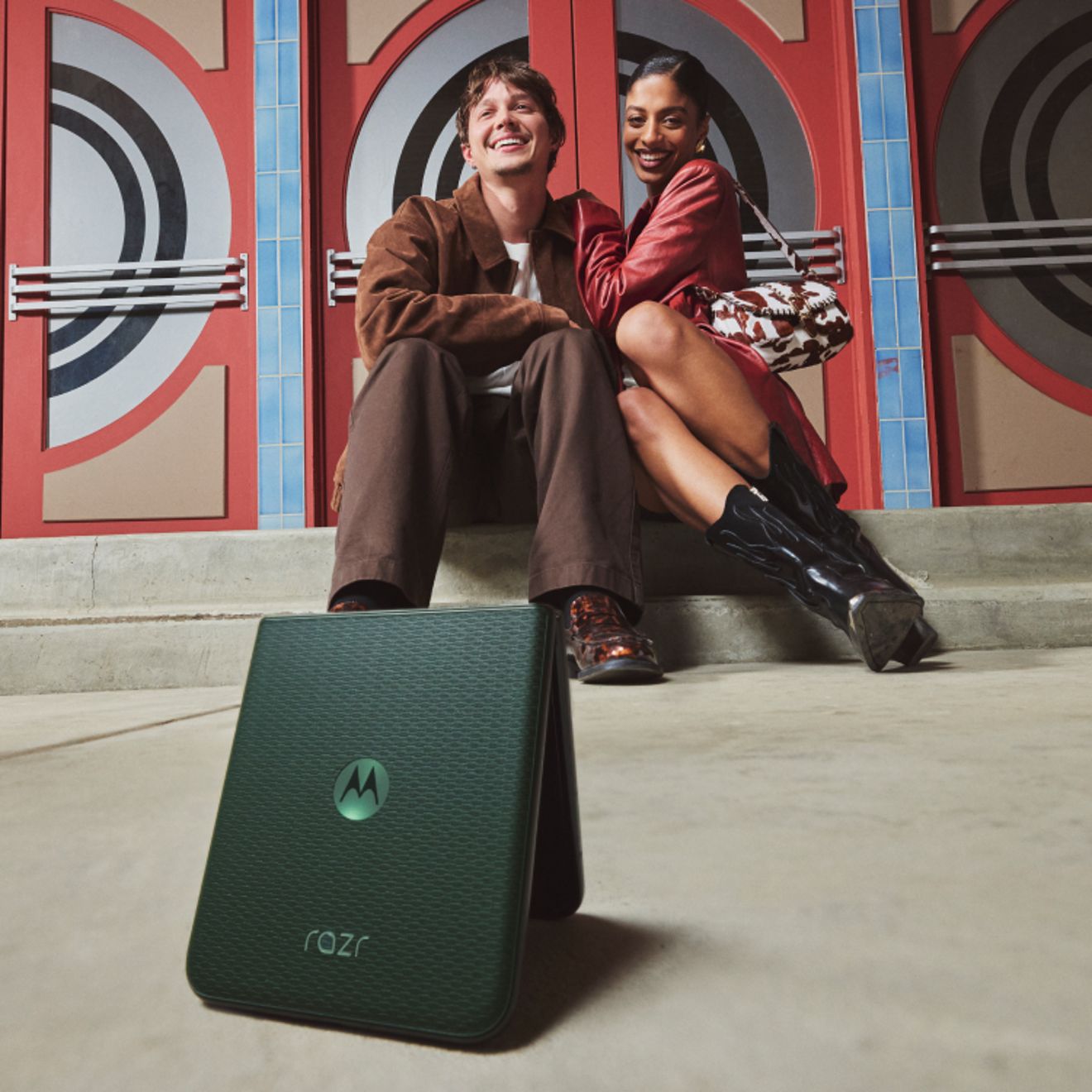 motorola razr in PANTONE® Mountain View shown in Flex View mode in the foreground, with two people sitting together and smiling in the background.