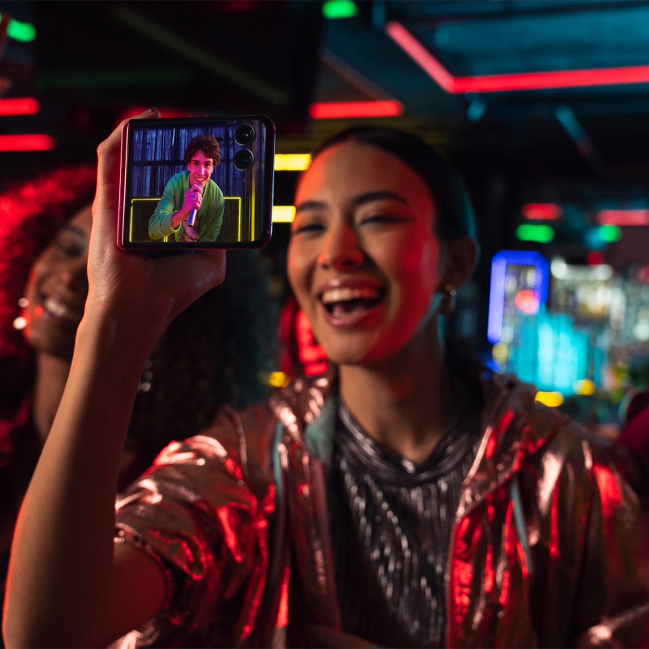 Person using motorola razr plus to take video of friend dancing at club with colorful lights.