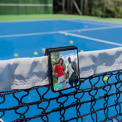 Motorola razr ultra folded over the top of a tennis court net to capture photo-booth selfie of two friends.