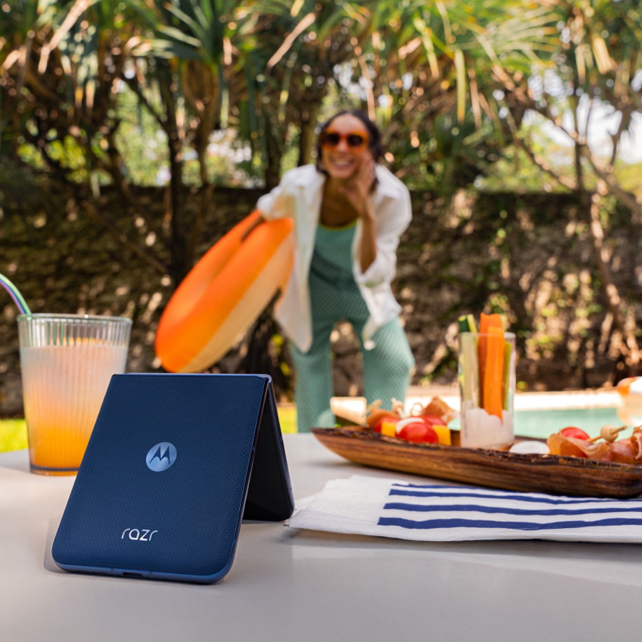 Person posing in front of motorola razr balanced on a table at a pool party.