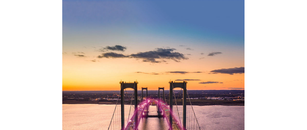 Magenta rays going through two hanging bridges at sunset.