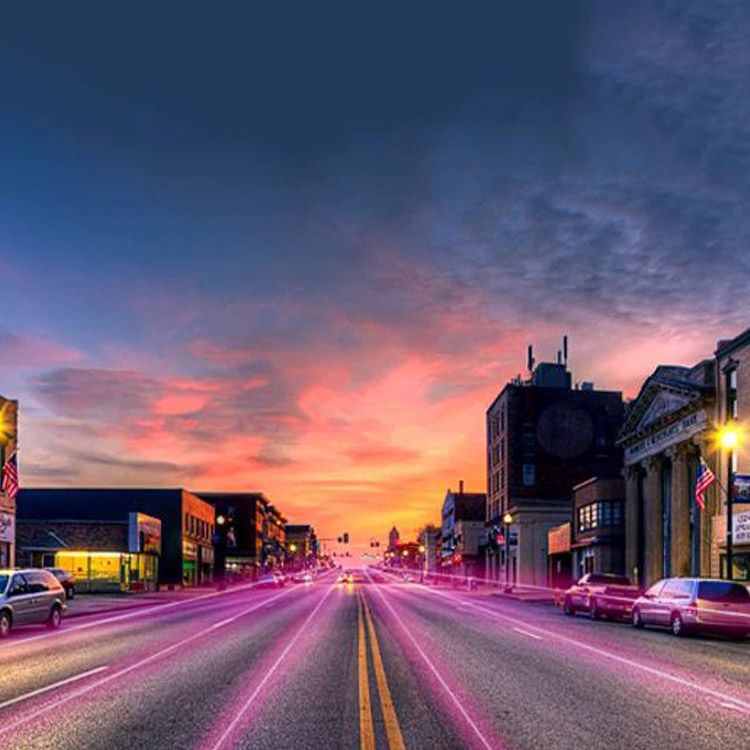 The main downtown street of a small town during sunset is lit up with magenta lines.