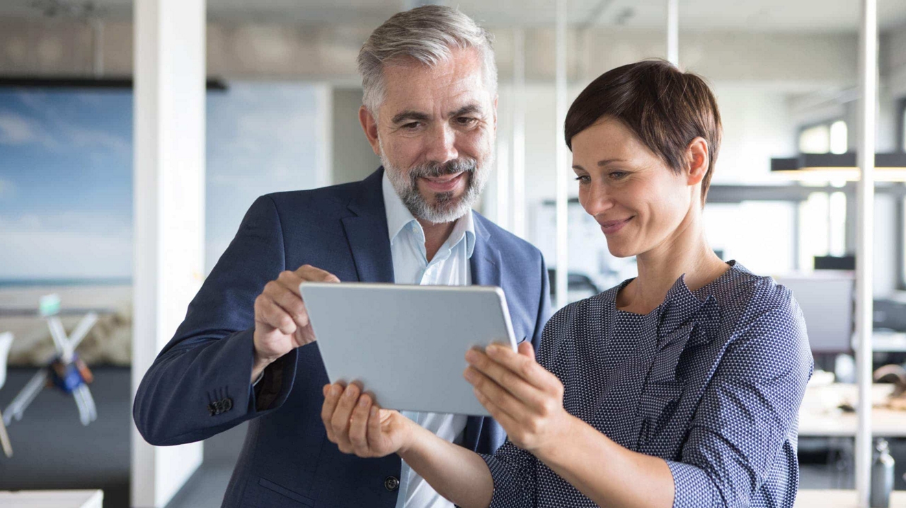 Two coworkers look at content on a 5G connected laptop while standing inside an open office. 