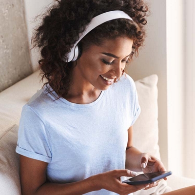 A sitting woman who’s wearing headphones, typing on her phone.