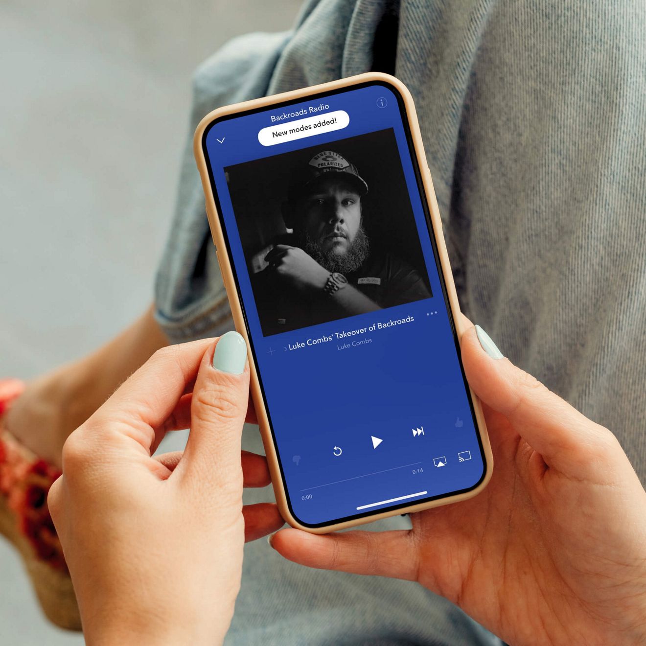 Hand holding a phone showing the Pandora app screen.