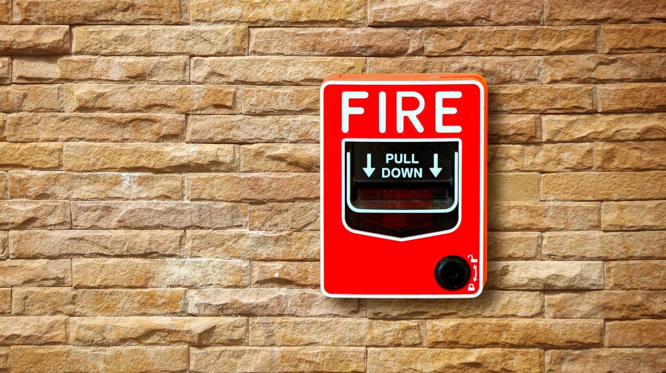 A fire alarm box hangs on a brick wall.