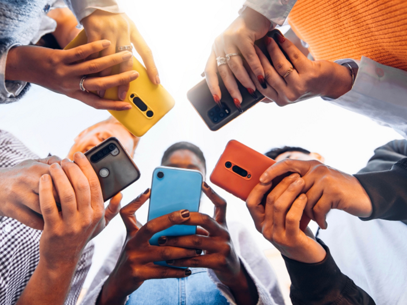 ​​A group of people standing in a circle, holding their phones so they resemble a starburst from below.​ 