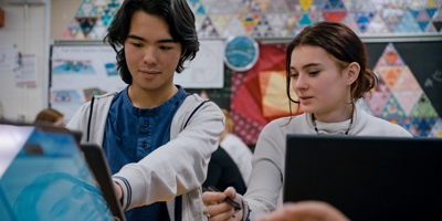 Two students doing classwork together on laptops.