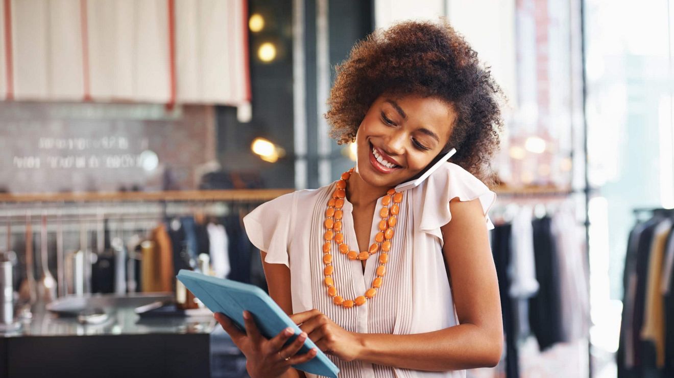 A retail store employee speaks on the phone and uses a connected tablet for business. 