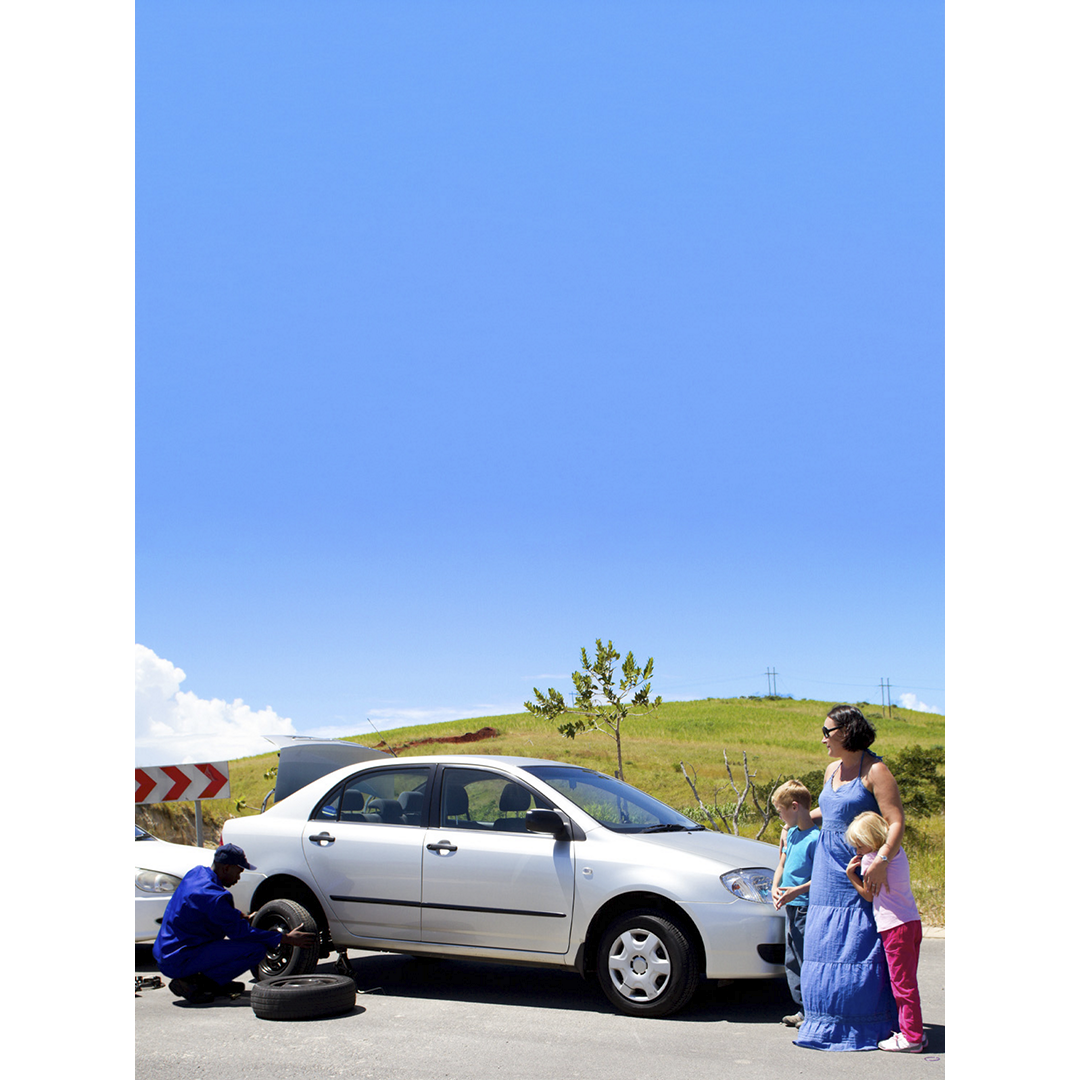 A family standing next to their car as a AAA employee changes their tire