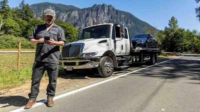 A tow truck driver levels the platform to transport a crashed vehicle. 