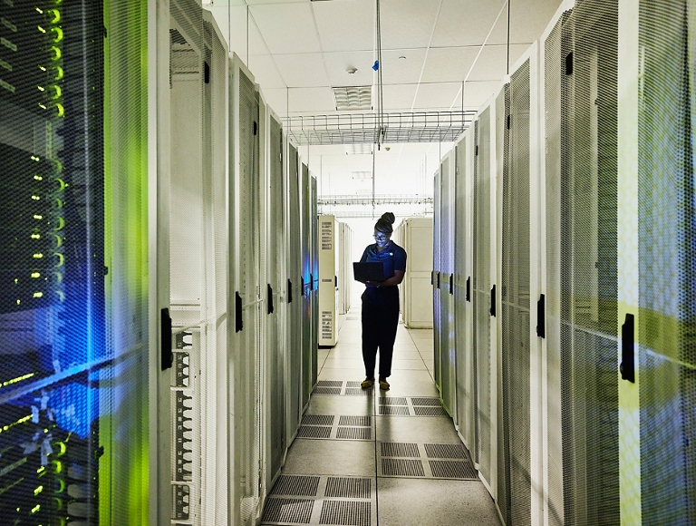 Person walking through a data center aisle with glowing server racks. 