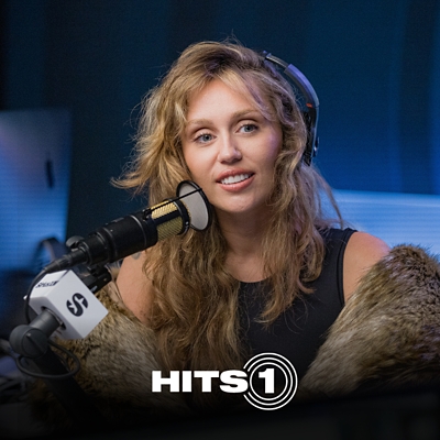 Musician, Miley, holding a microphone while smiling.