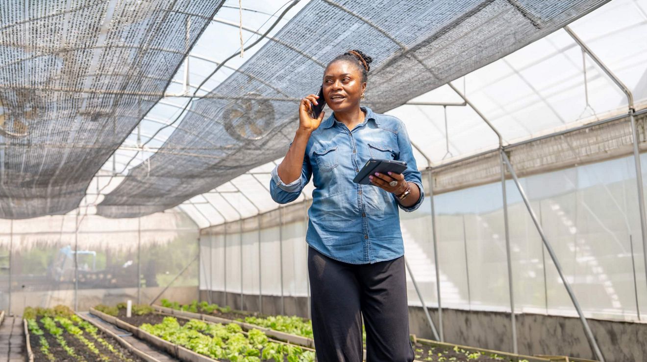 An agricultural manager talks on a smartphone while holding a tablet in a Metrolina Greenhouse.