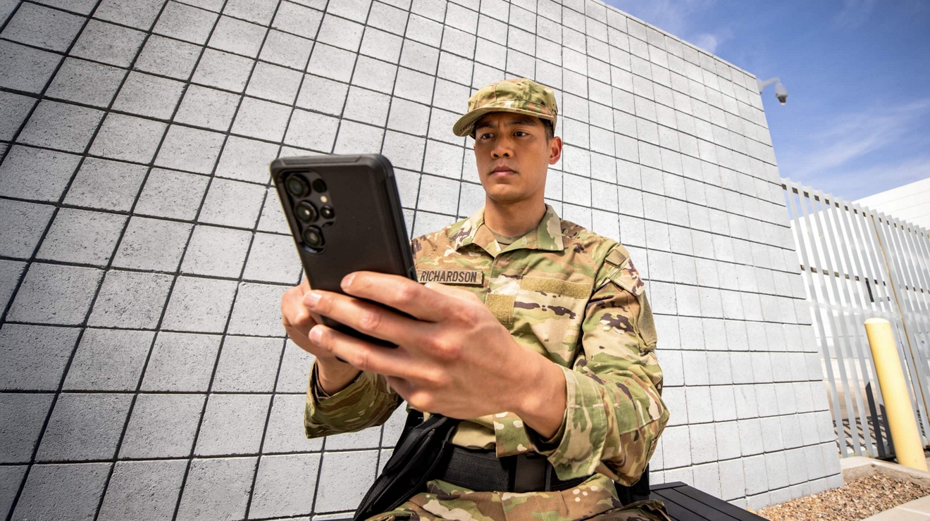 A uniformed guard at a facility gate checks their smartphone.