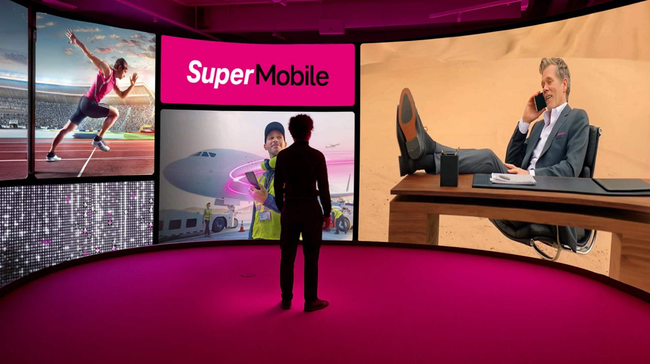 A businessperson stands in a digital theater, experiencing a floor-to-ceiling SuperMobile ad display.