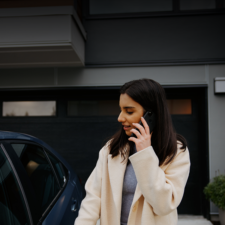 Mujer hablando por teléfono al lado de su auto.