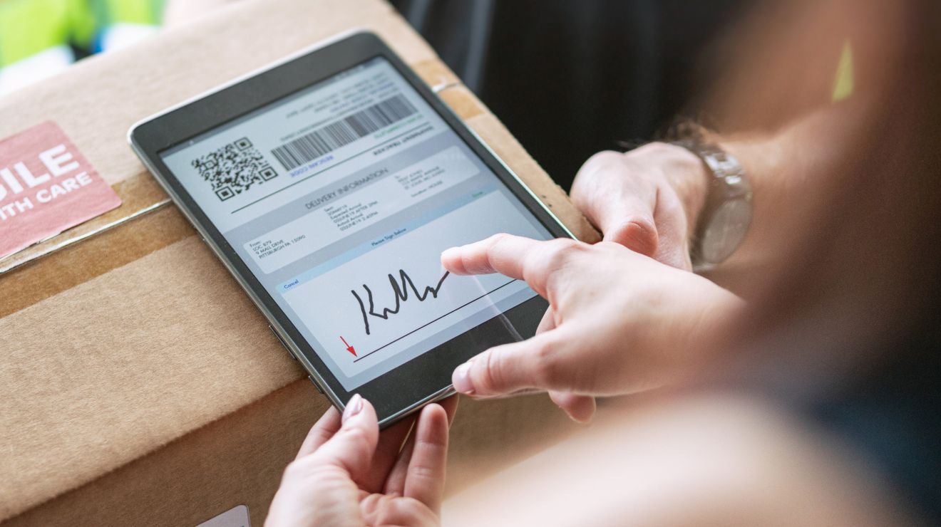 Driver confirms delivery with a customer by asking them to sign on a tablet.