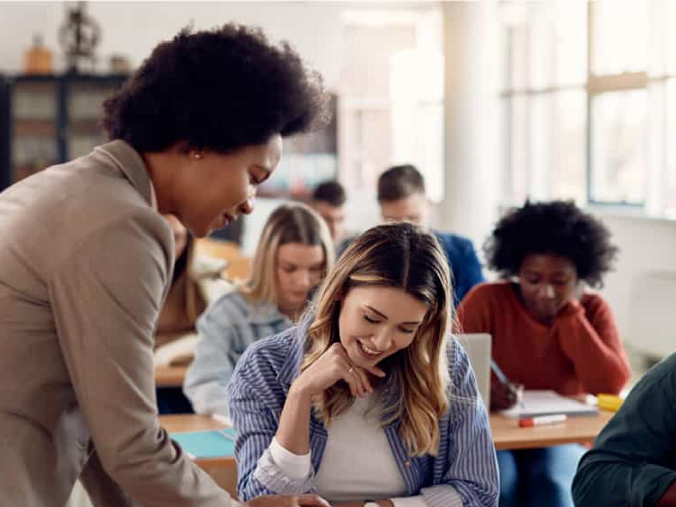 Classroom scene with students studying and a teacher assisting.