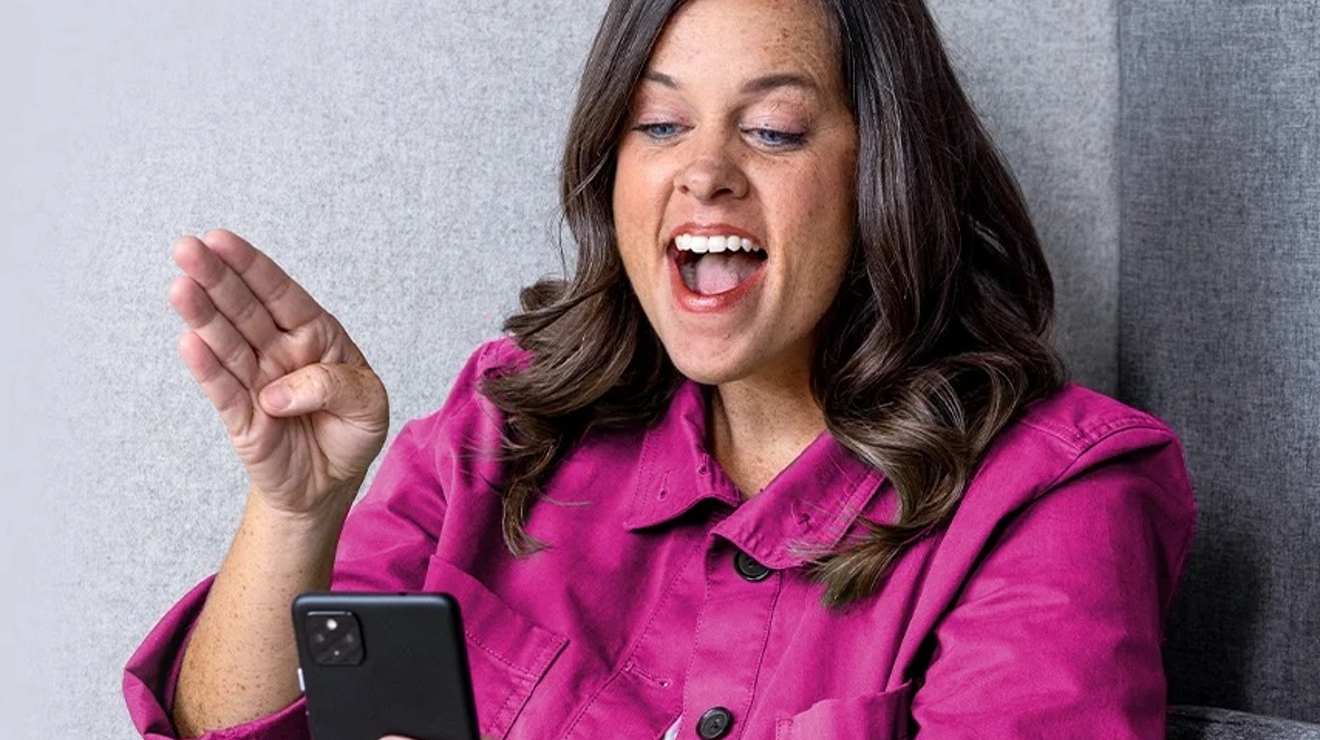 Woman wearing a magenta coat while laughing on cellphone call.