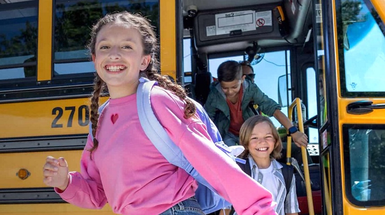 Girl wearing a pink sweatshirt smiling as she exits a school bus.