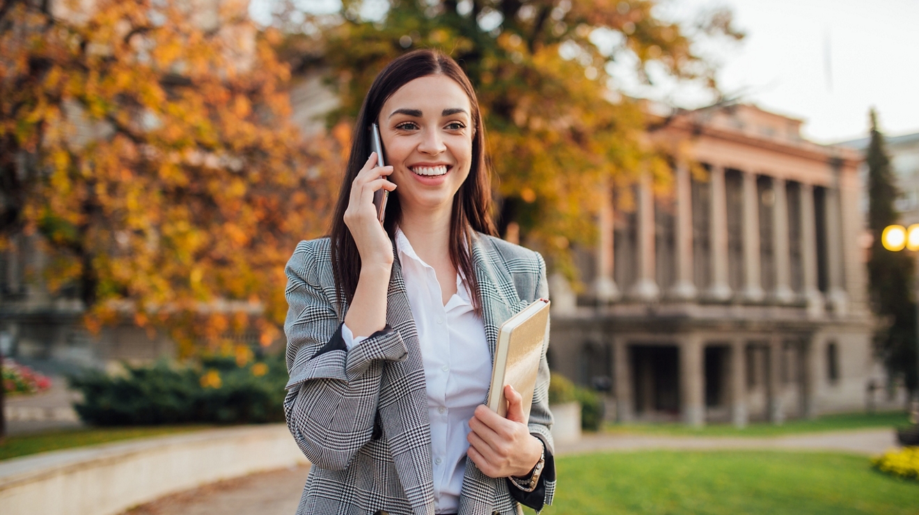 Young woman looking happy while talking on cellphone outside of university building.