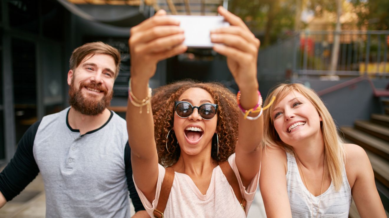 Three friends smiling and taking a selfie outdoors.